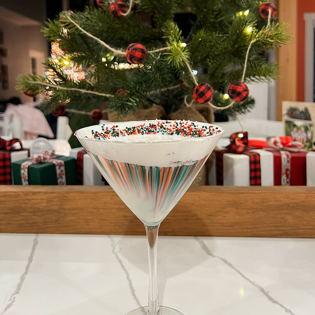 Creamy white peppermint martini in a glass rimmed with marshmallow fluff and red and green Christmas sprinkles.